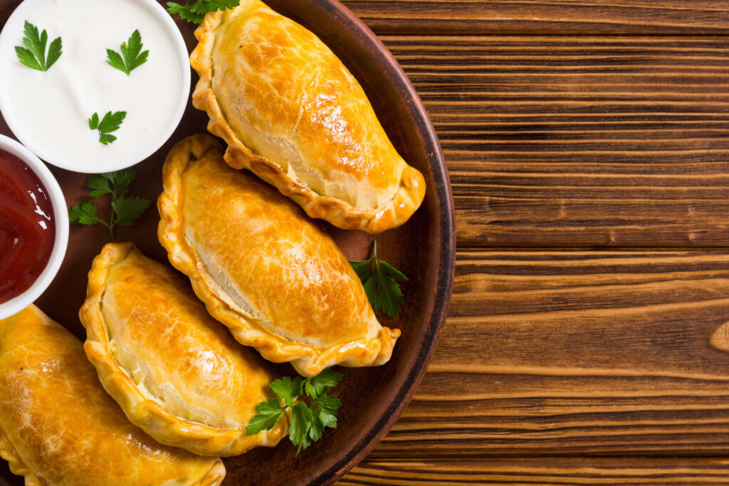Golden baked empanadas on a rustic plate with sour cream and dipping sauce